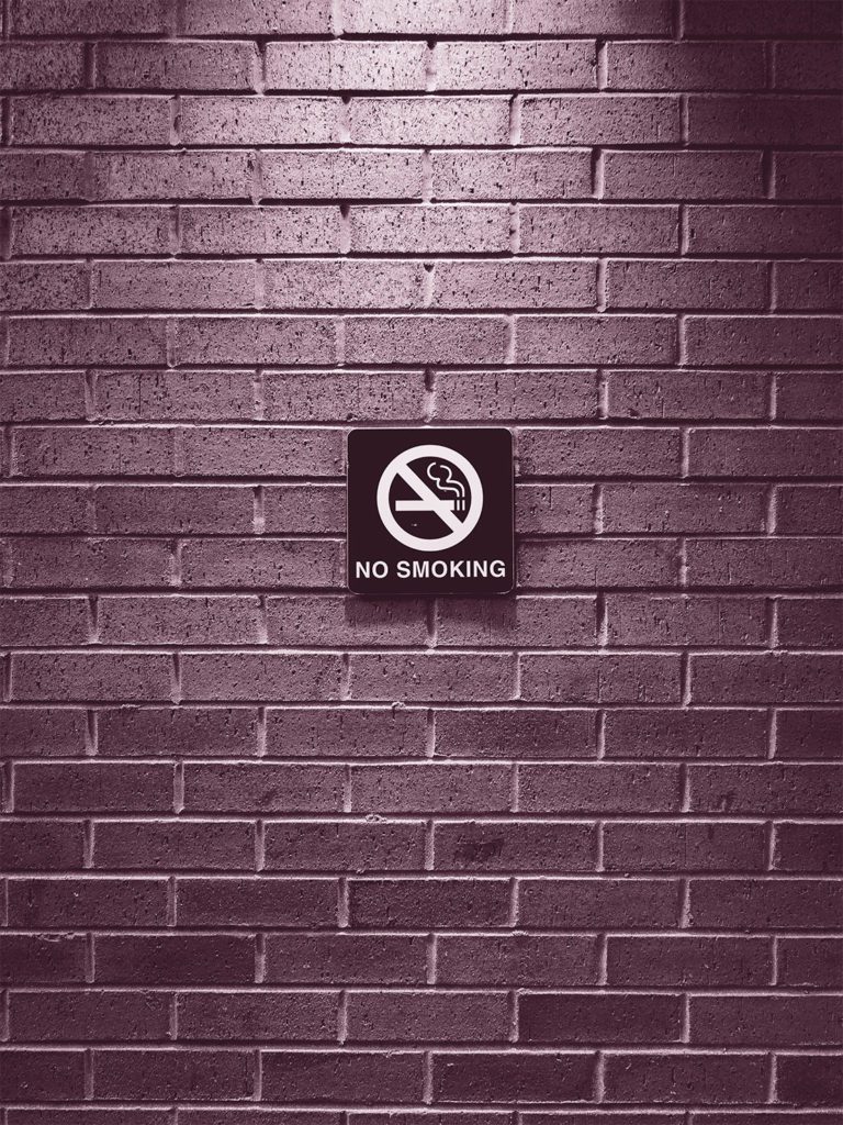 Habits that May Lead to Breast Cancer; pink overlay on image of a brick wall with a no smoking sign