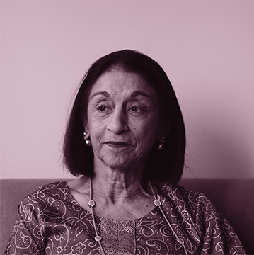 breast cancer in older adults; an indian woman in her upper 50s to younger 60s is facing just barely off to the left of the camera. She has a faint smile and is wearing a paisley patterned shirt, a beaded necklace, and simple earrings. The whole image has a pink filter.